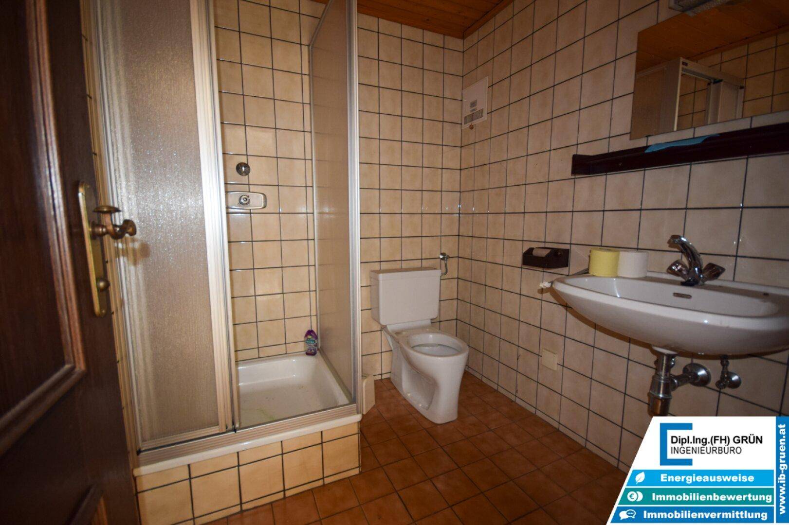 Kleines Badezimmer mit Duschkabine, WC, Waschbecken und beigefarbenen Fliesen.