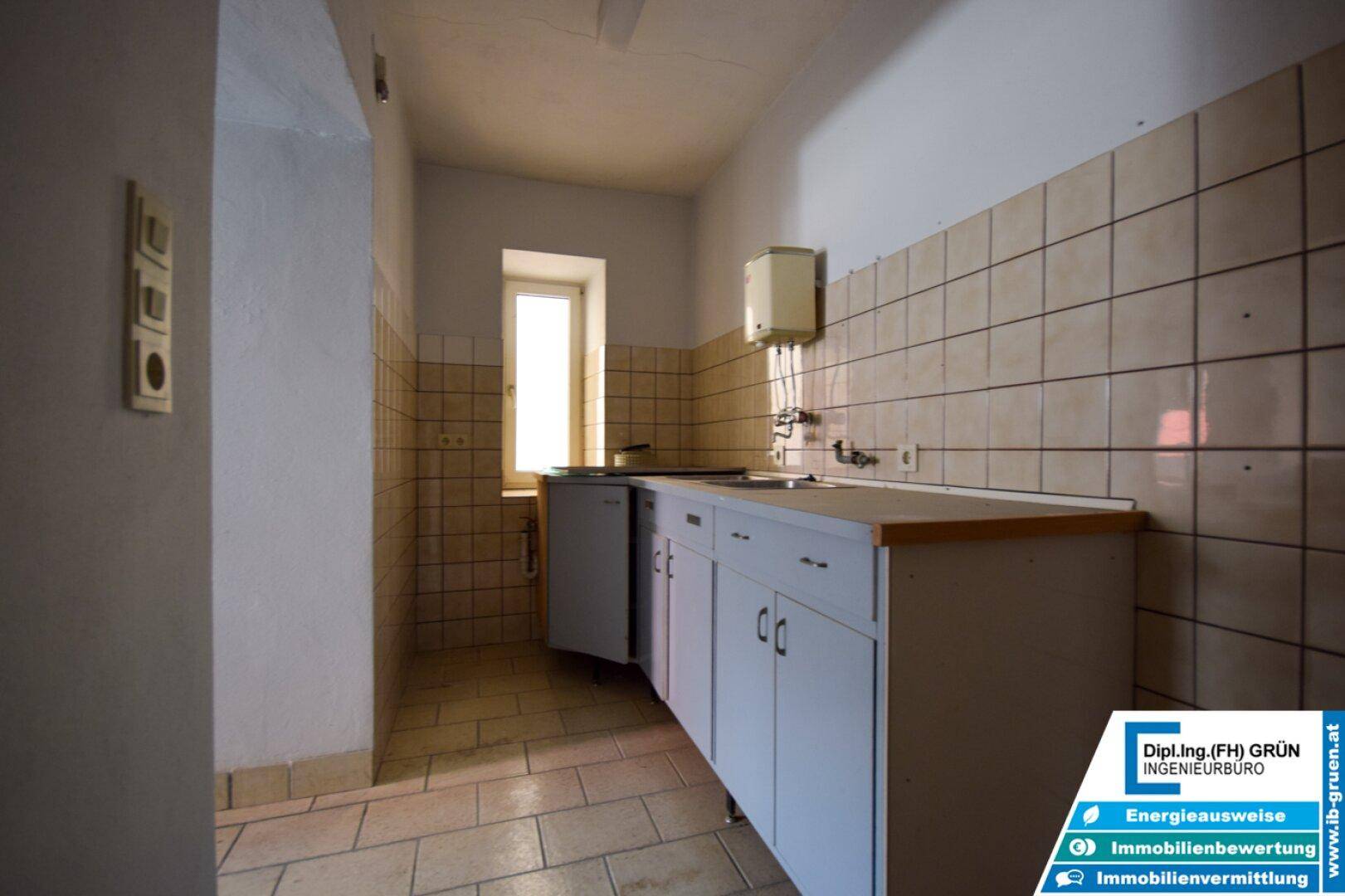 Kleine Küche mit weißen Unterschränken, Fliesenwand und einem schmalen Fenster.