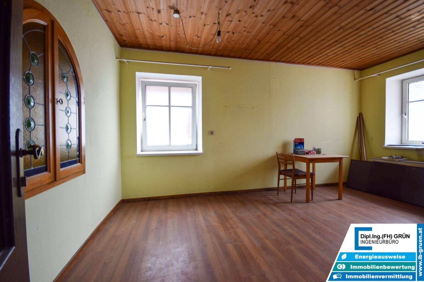 Großer Raum mit Holzdecke, Holzboden und einem dekorativen Buntglasfenster.