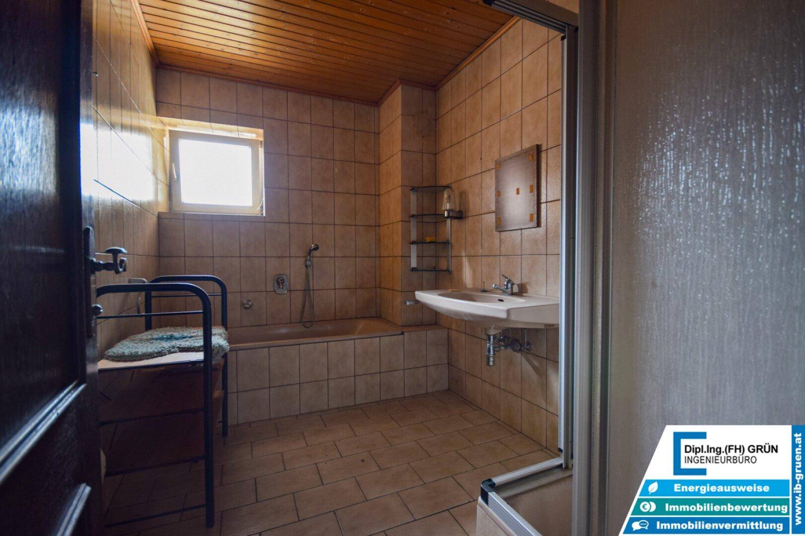 Badezimmer mit beigefarbenen Fliesen, Badewanne, Waschbecken und Holzdecke.