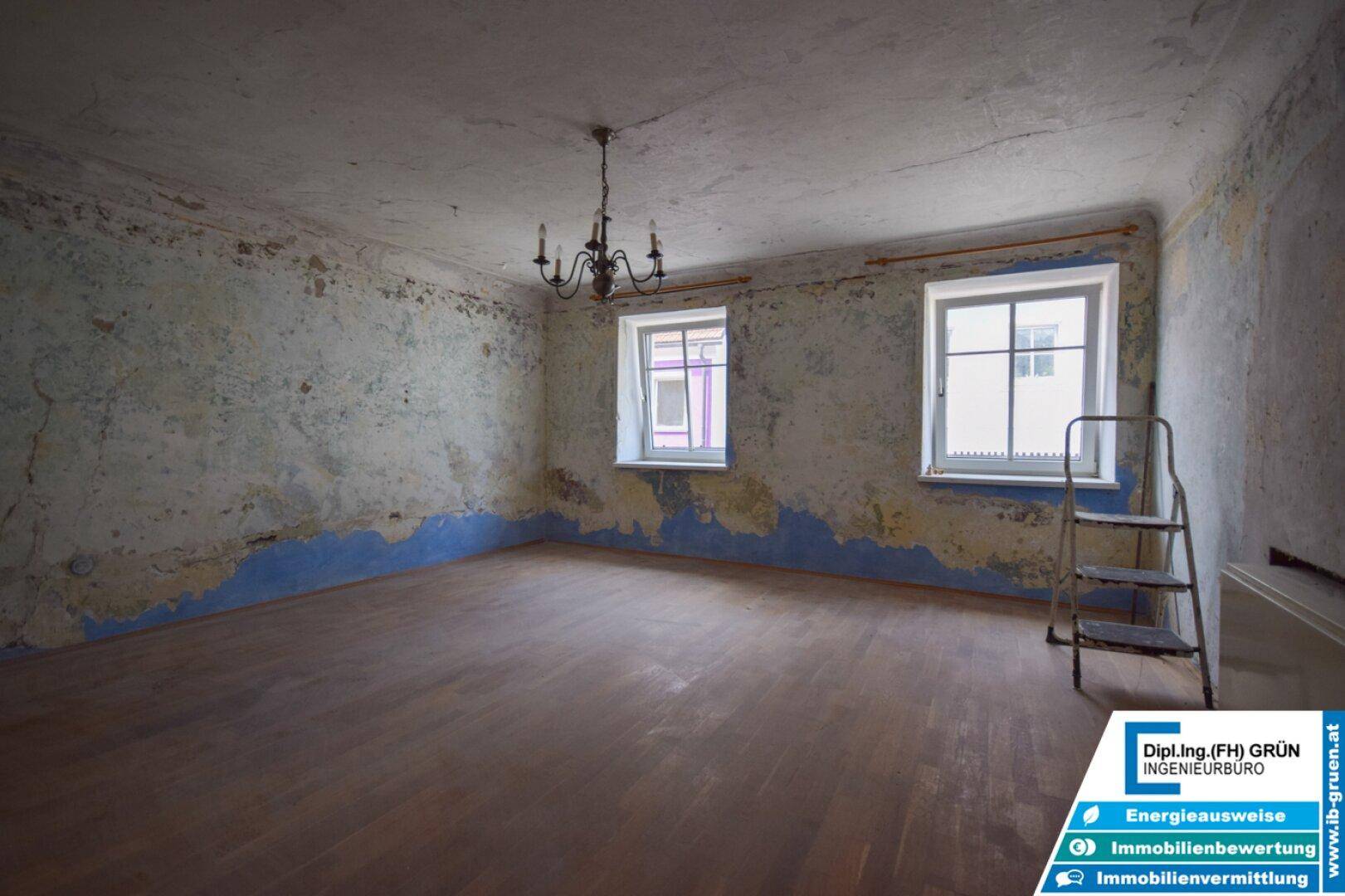 Großer, renovierungsbedürftiger Raum mit abblätternder Farbe und Holzboden.
