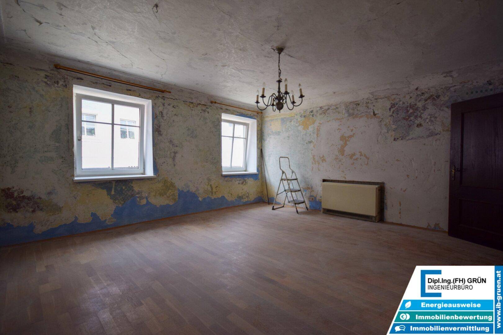 Renovierungsbedürftiger Raum mit abblätternder Farbe, Holzboden und einem Heizkörper.