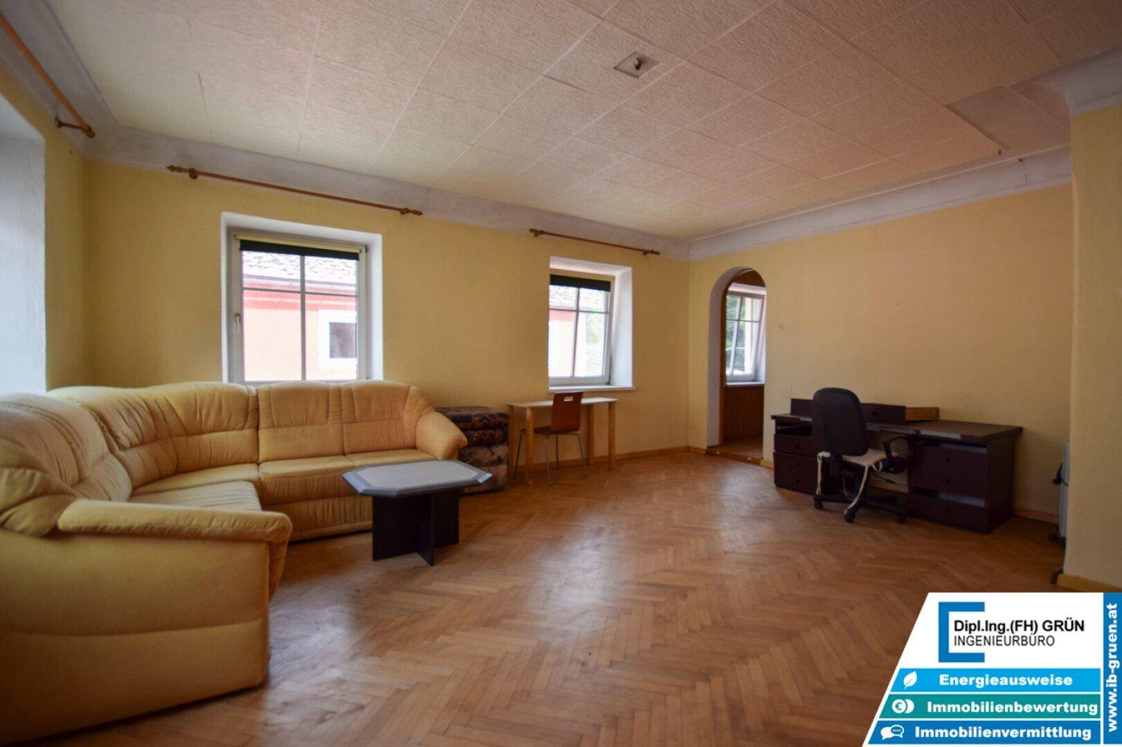 Geräumiges Wohnzimmer mit Fischgrätparkett, gelben Wänden und einem Sofa.