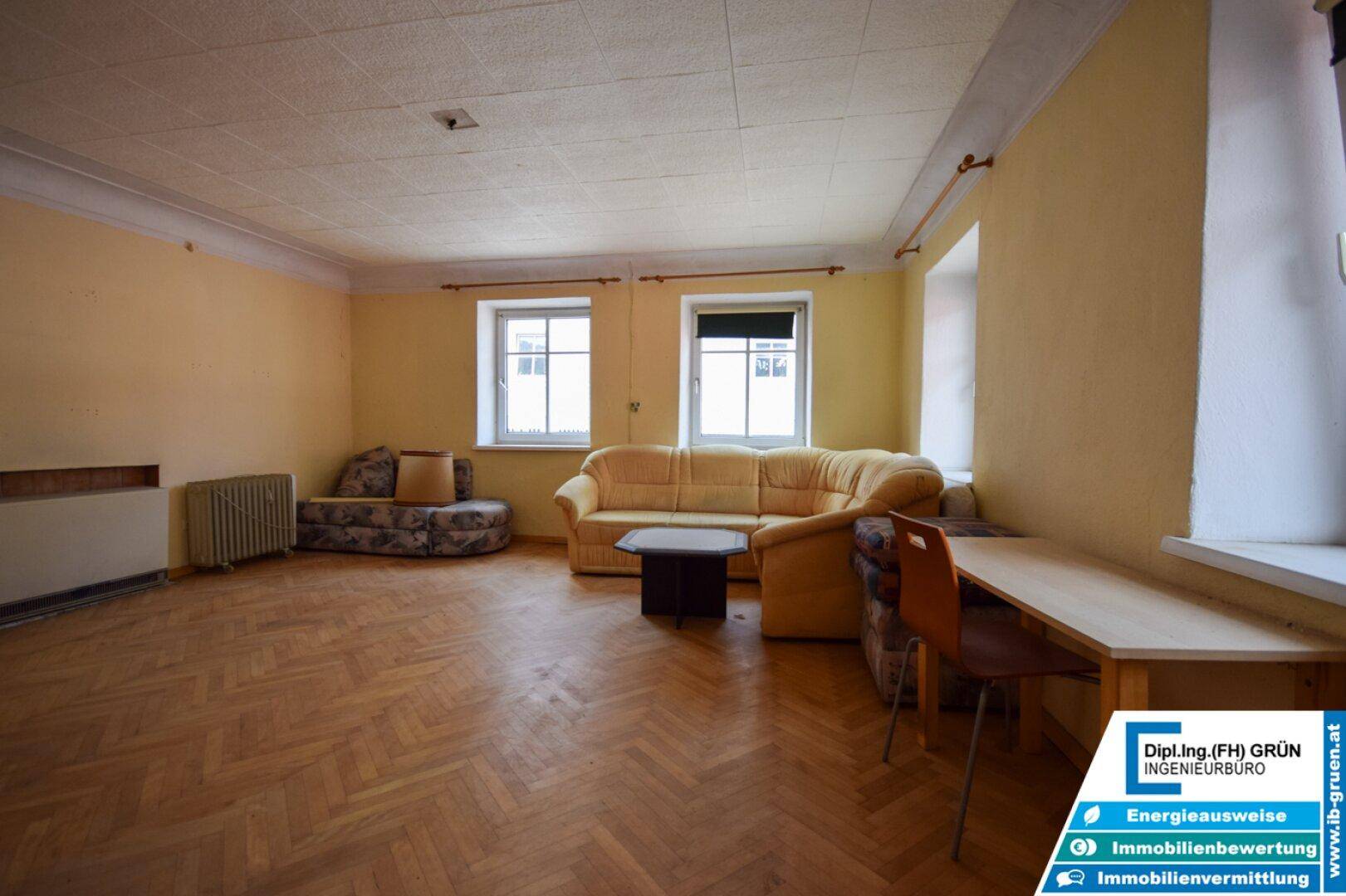 Helles Wohnzimmer mit Fischgrätparkett, gelben Wänden und traditionellen Heizkörpern, in gutem Originalzustand.