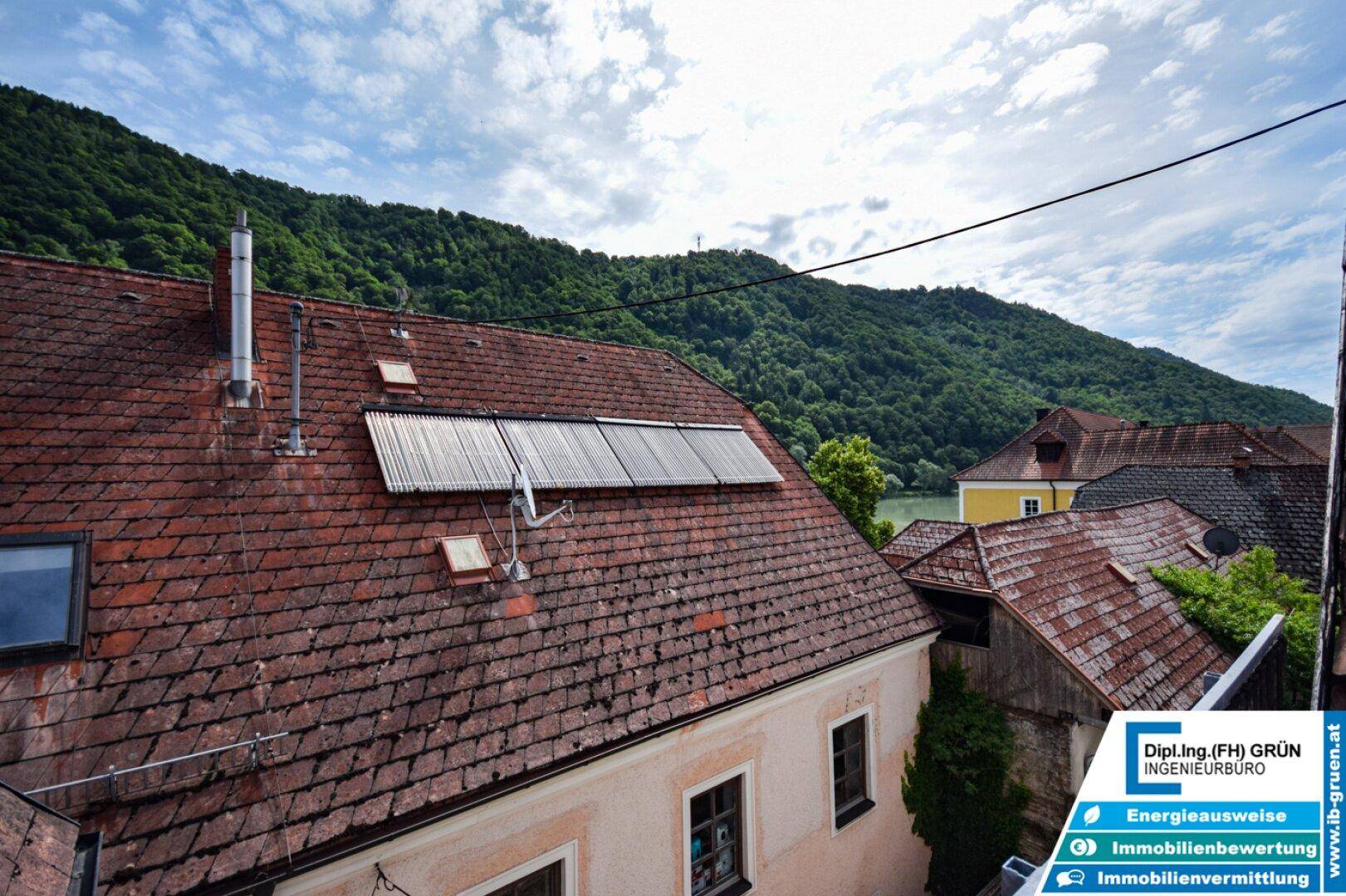Dachlandschaft mit Ziegeln und Solarpaneelen, bietet einen weiten Blick auf einen Fluss und grüne Hügel.