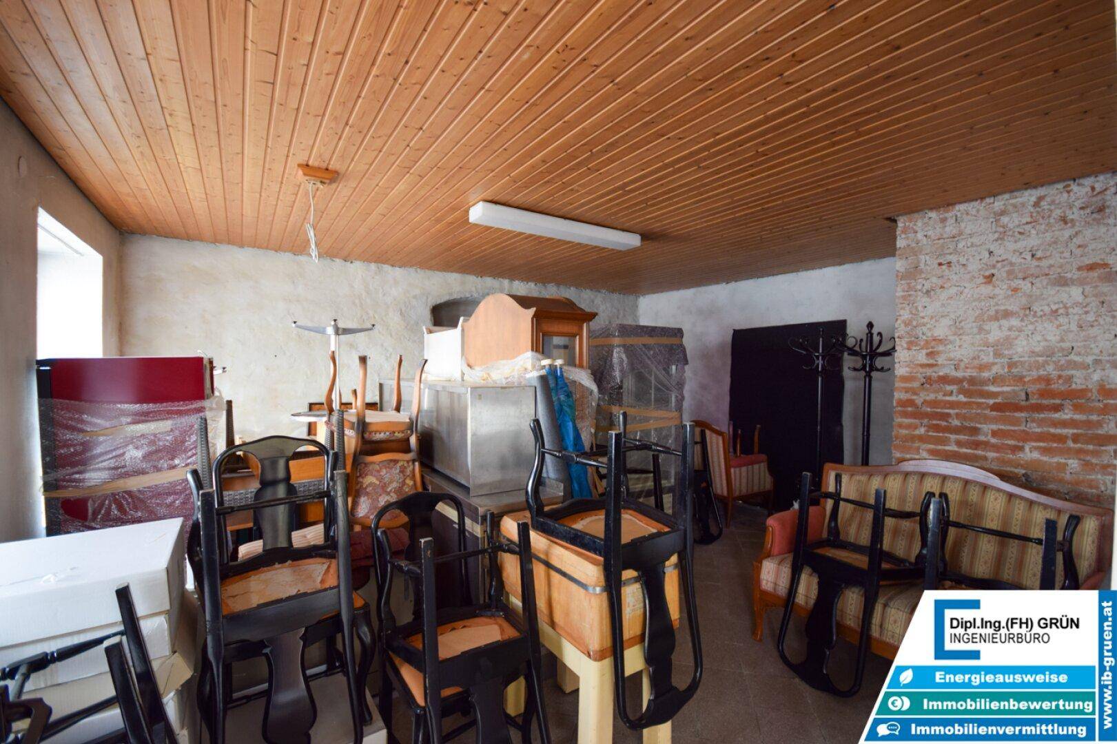 Lagerraum im Keller mit Holzpaneeldecke, Betonwänden und gestapelten Möbeln und Gegenständen.