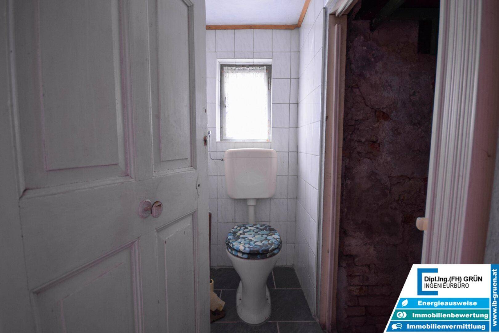 Kleines WC mit Fliesenboden, Fenster und einem traditionellen Toilettenbecken.