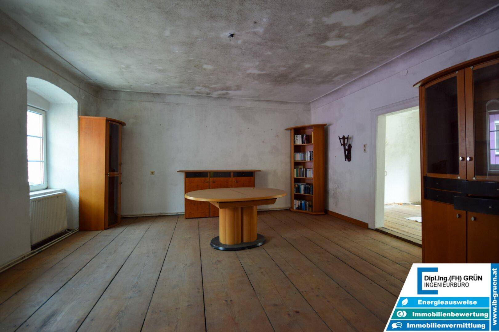 Geräumiger Wohnraum mit Holzdielenboden, einem ovalen Tisch und Holzschränken.