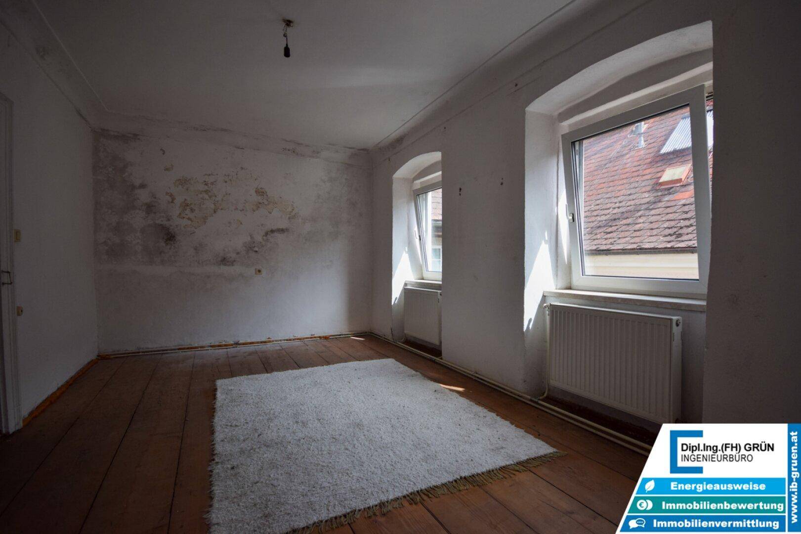 Helles Schlafzimmer mit Holzdielenboden, Fenstern und einem gemütlichen weißen Teppich.