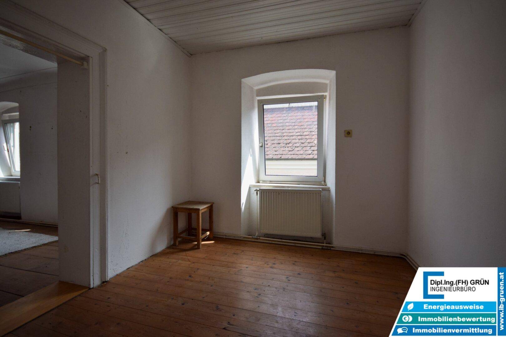 Kleiner Raum mit Holzdielenboden, einem Fenster und einem Beistelltisch.