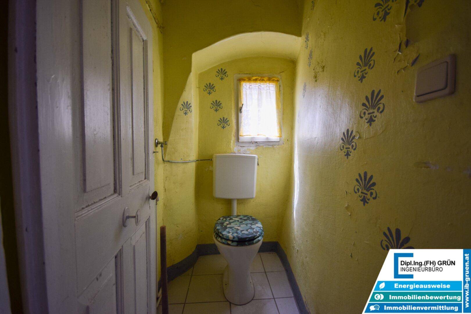 Kleines WC mit gelben Wänden, Fliesenboden und einem Fenster.