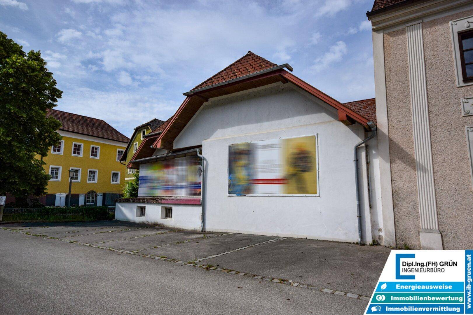 Seitenansicht eines Gebäudes mit weißer Fassade, roten Dachziegeln und einem Parkplatz davor.
