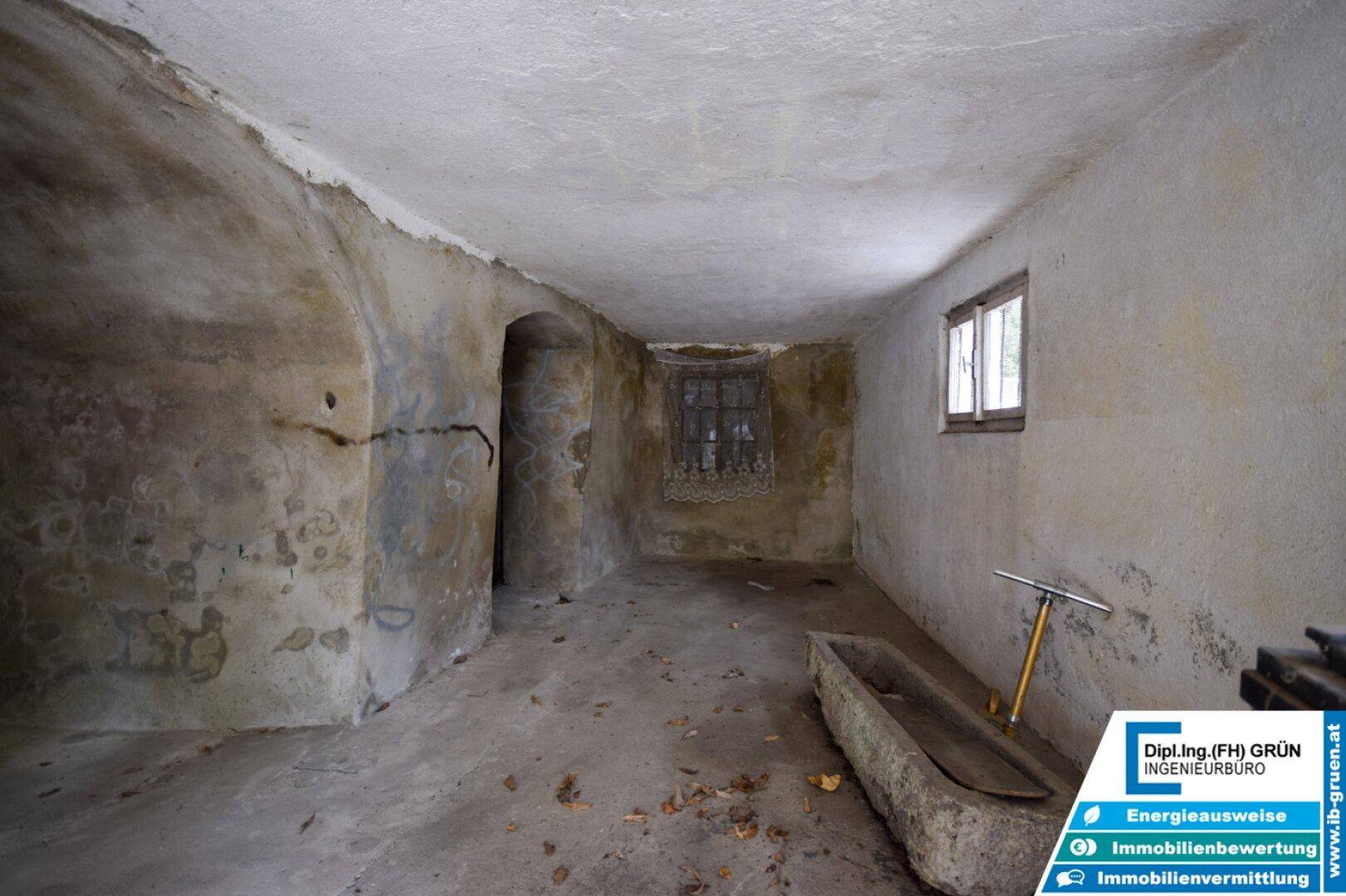 Alter Kellerraum mit gewölbter Decke, kleinen Fenstern und einem steinernen Trog.
