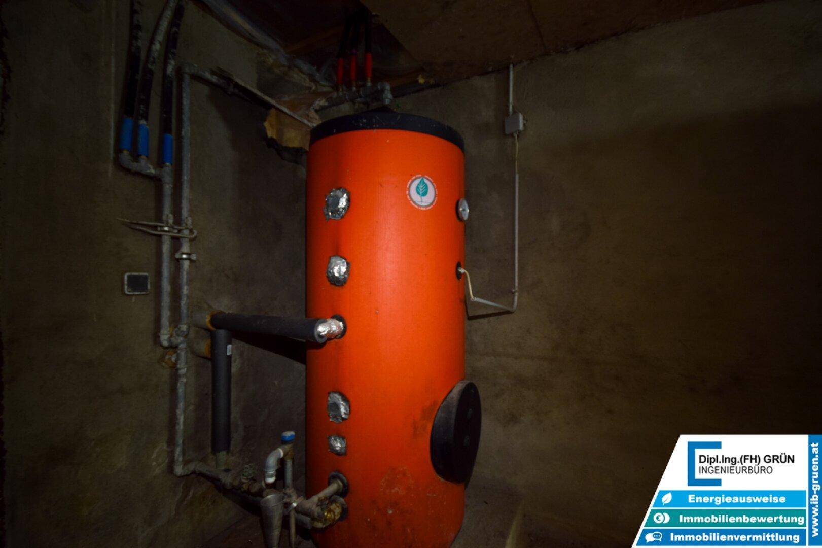 Großer oranger Warmwasserspeicher mit Rohren und Anschlüssen in einem Technikraum.