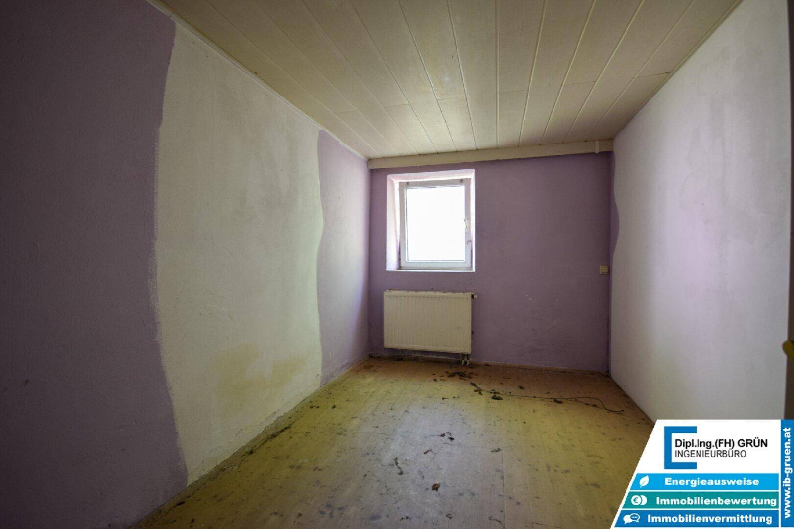 Einfaches Zimmer mit lila und weißen Wänden, einem Fenster und einem Heizkörper.