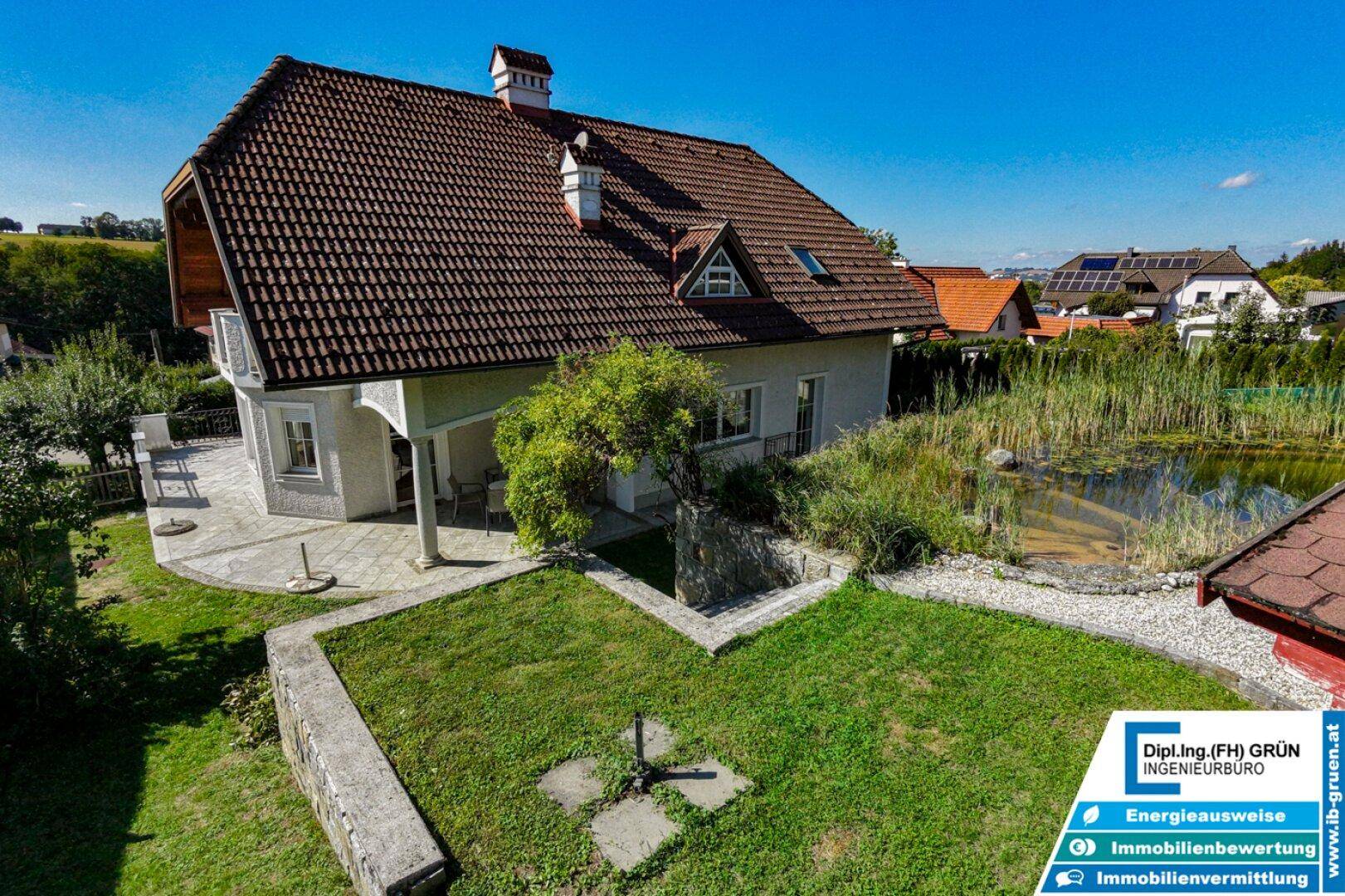 Haus mit gepflegtem Garten, Rasenfläche und Teich von erhöhter Perspektive.