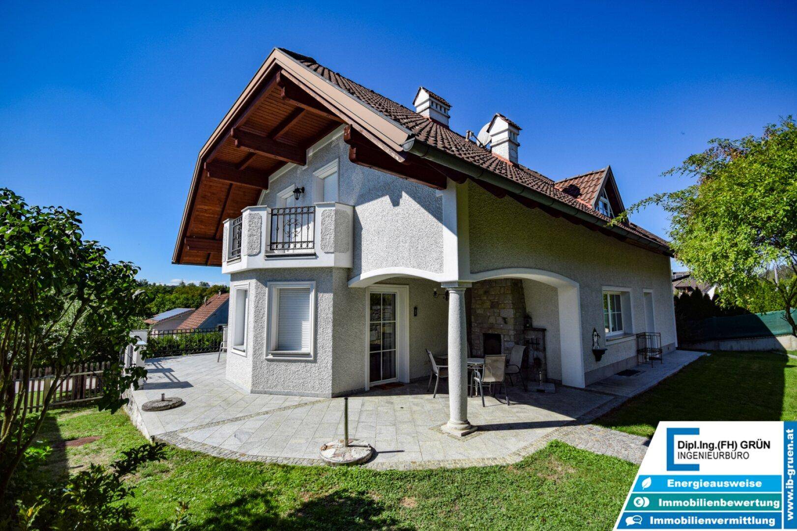 Hausfassade mit überdachter Terrasse und kleinem Balkon unter blauem Himmel.