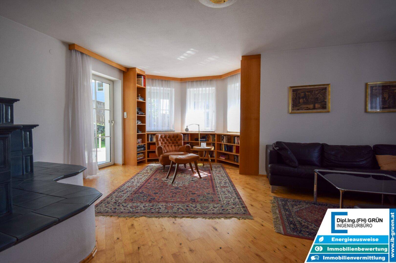 Geräumiges Wohnzimmer mit Holzboden, Kachelofen und vielen Fenstern für natürliches Licht.