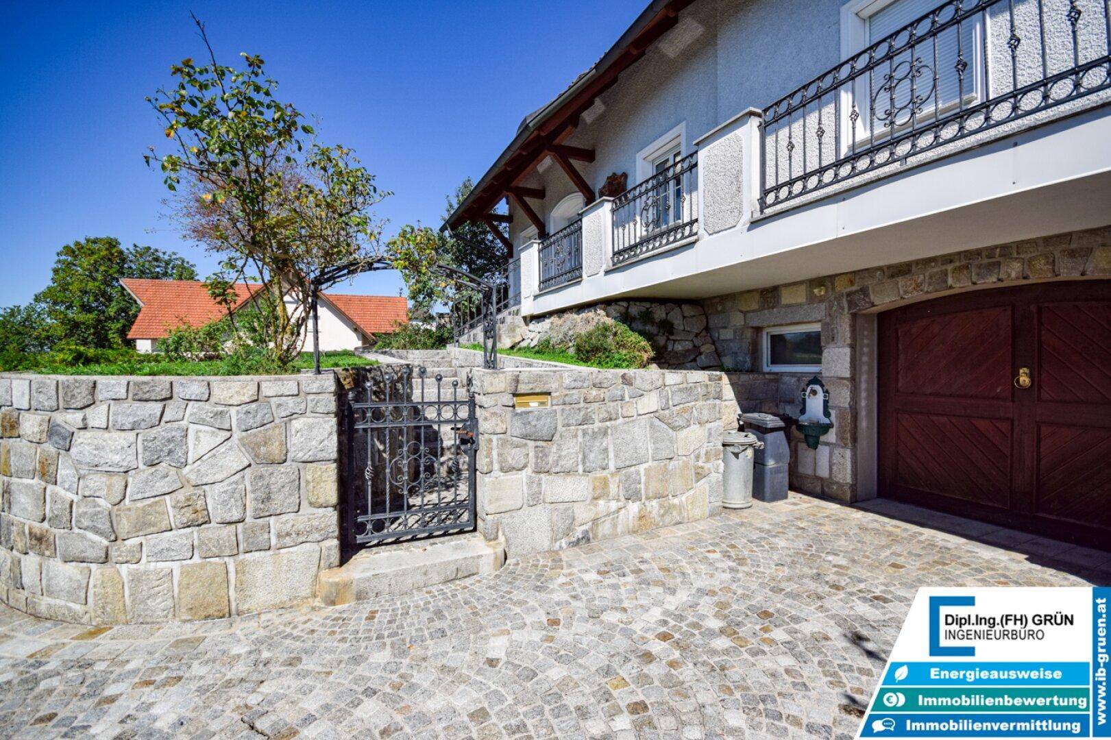 Gepflasterte Auffahrt zum Haus mit Natursteinmauern und Garagentoren.