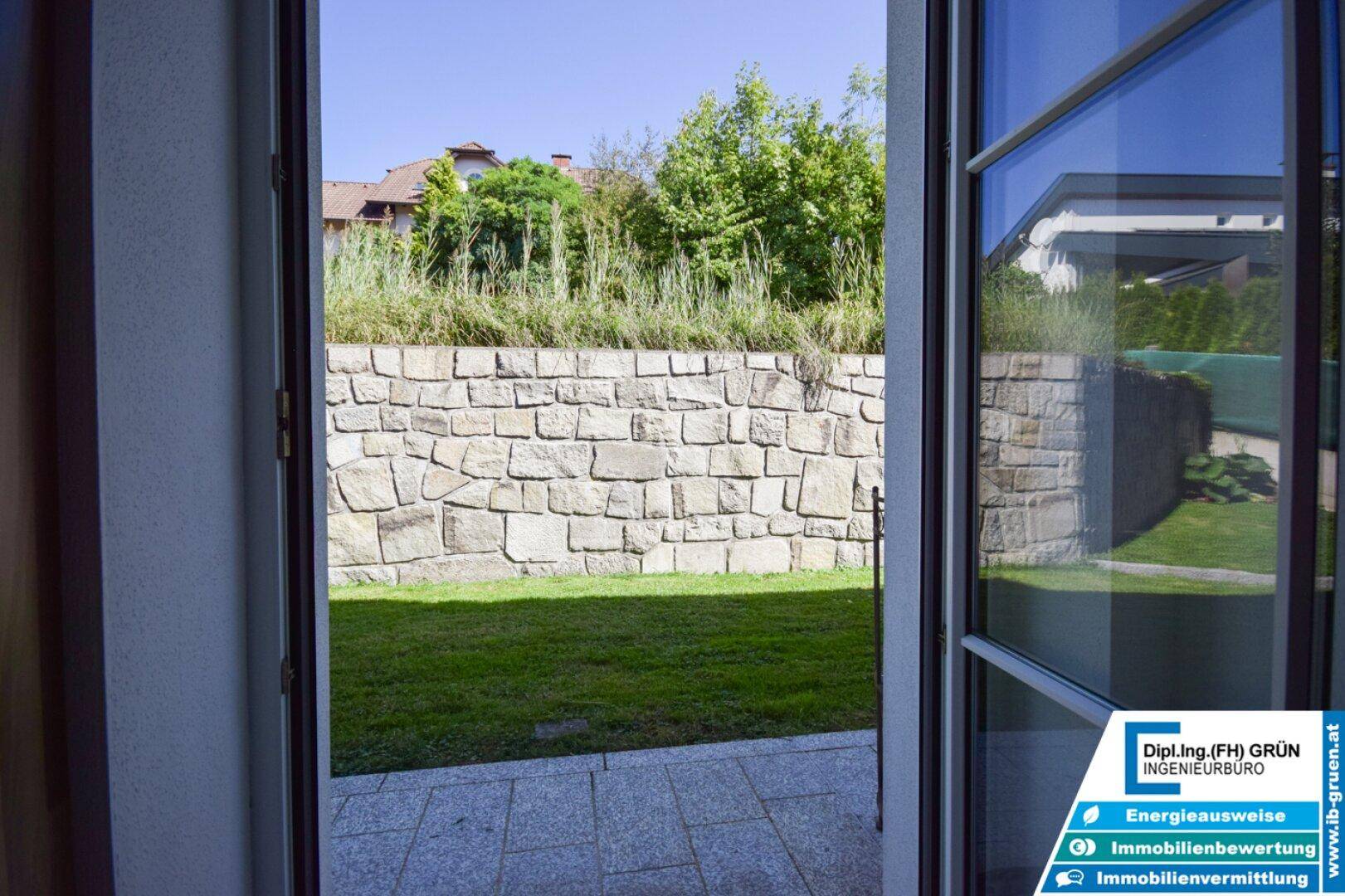 Blick vom Haus auf eine kleine Rasenfläche mit Natursteinmauer.