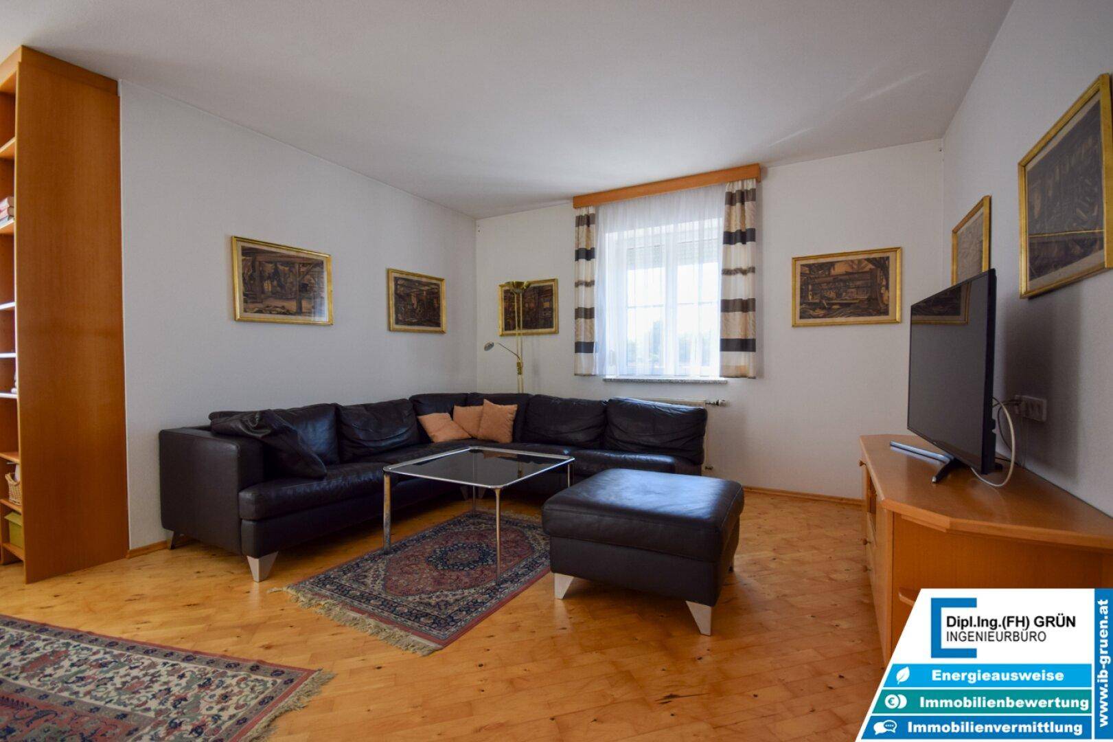 Gemütliches Wohnzimmer mit Ledersofa, Holzboden und Blick ins Grüne.