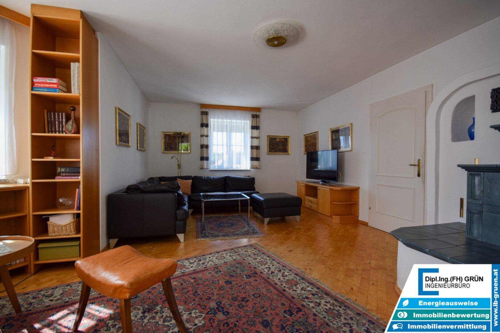 Geräumiges Wohnzimmer mit Ledersofa, Holzboden und traditionellem Kachelofen.