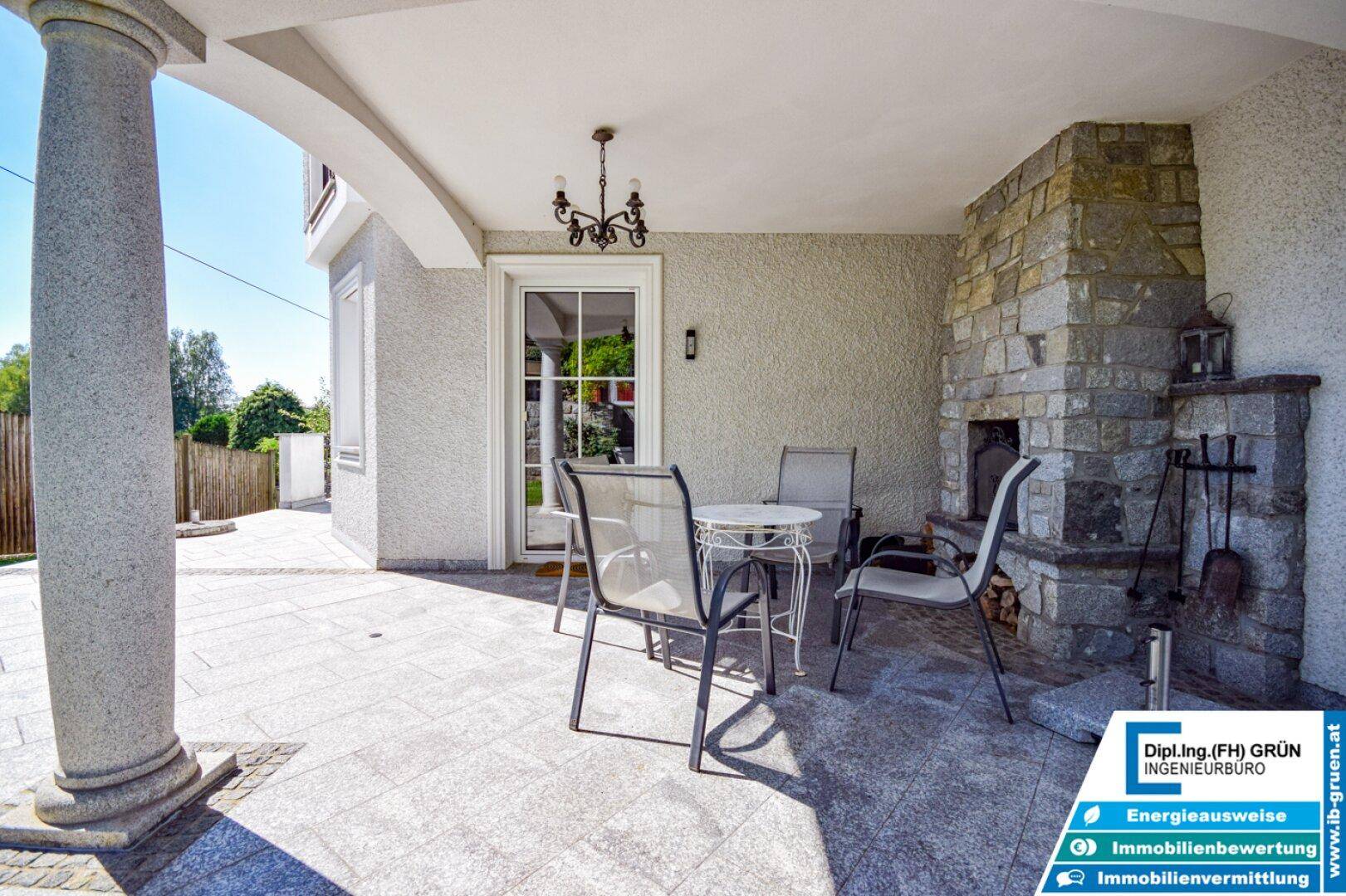 Große überdachte Terrasse mit Steinkamin und Gartenblick.