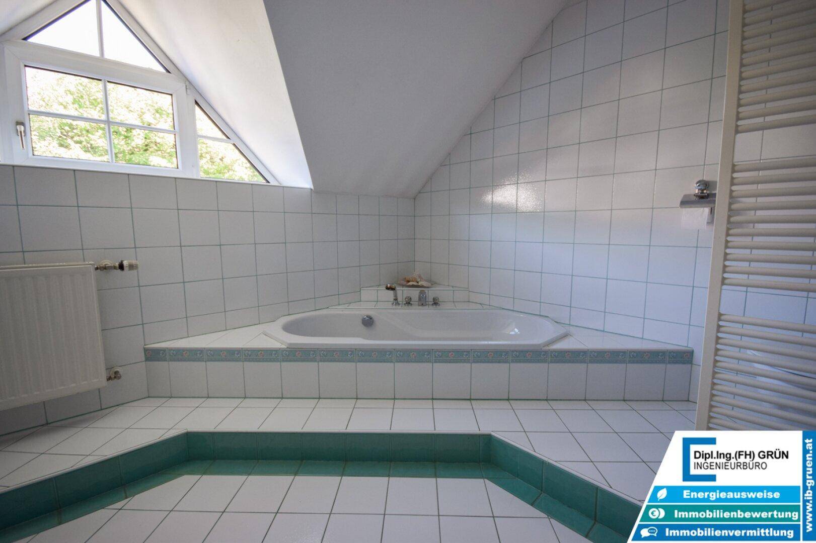 Eckbadewanne im Badezimmer mit weiß-grünen Fliesen und Dachschräge.