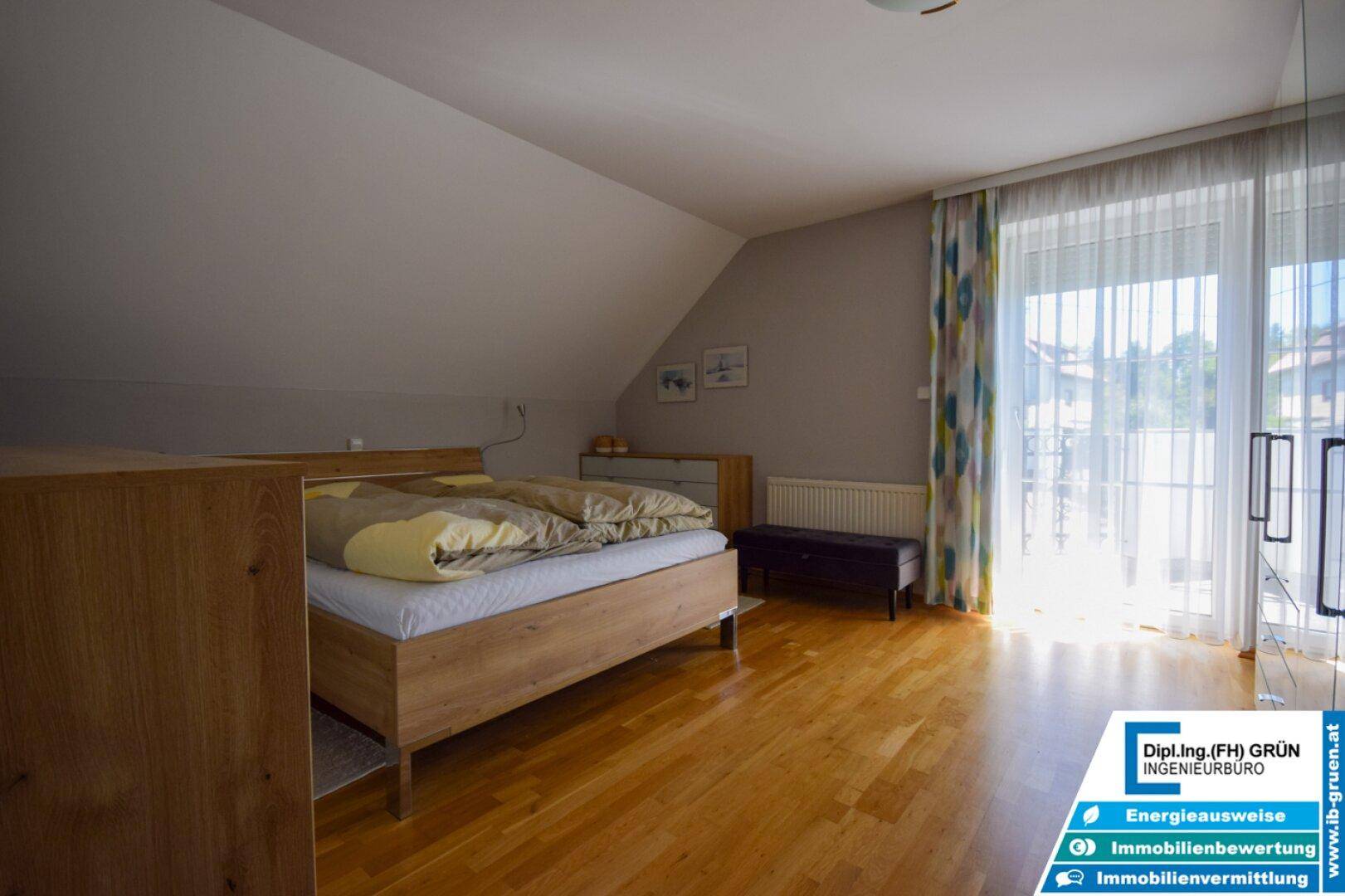 Helles Schlafzimmer im Dachgeschoss mit Holzboden und Zugang zum Balkon.