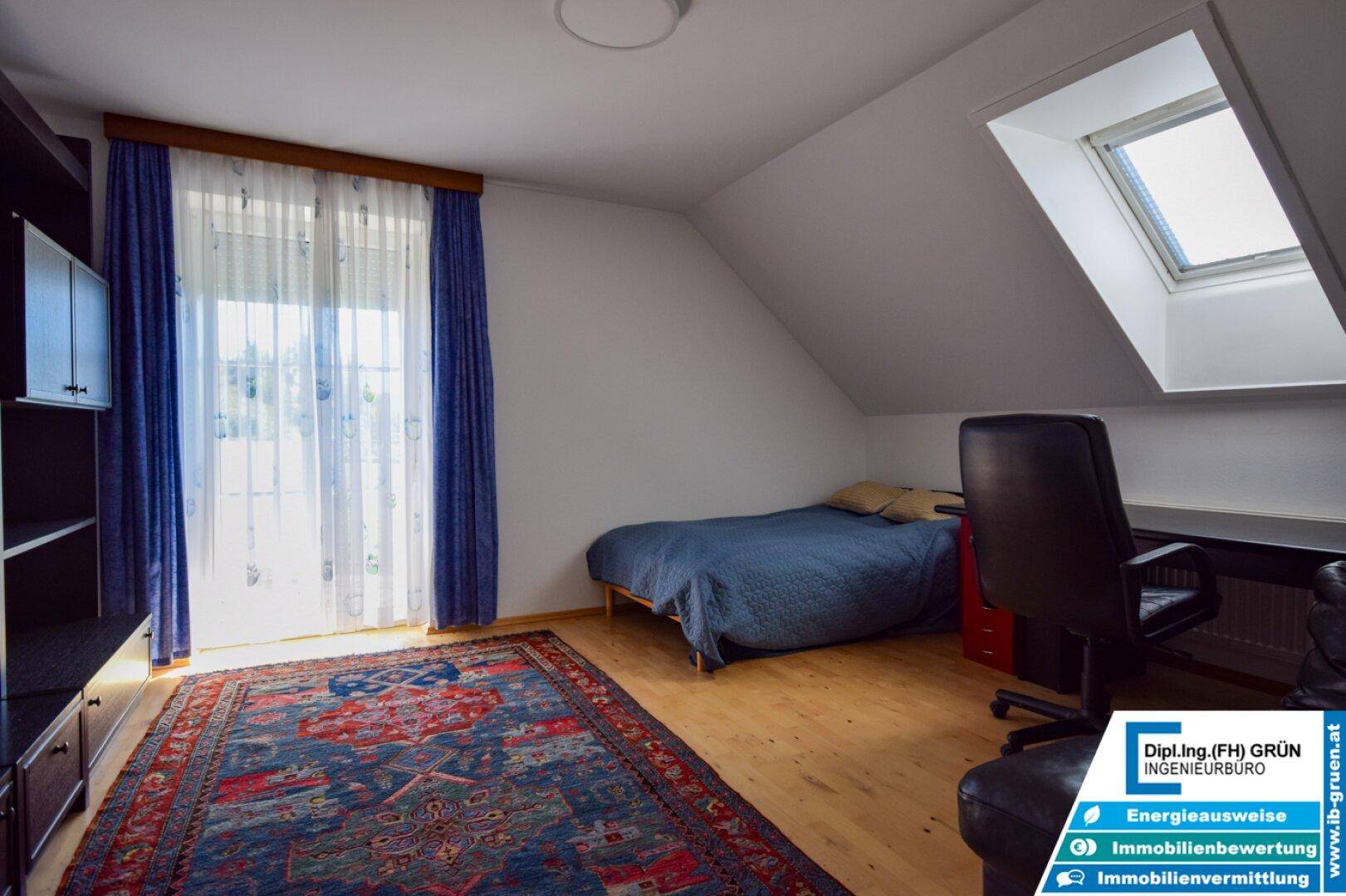 Gemütliches Schlafzimmer im Dachgeschoss mit Holzboden, Bett und Schreibtisch unter einem Dachfenster.