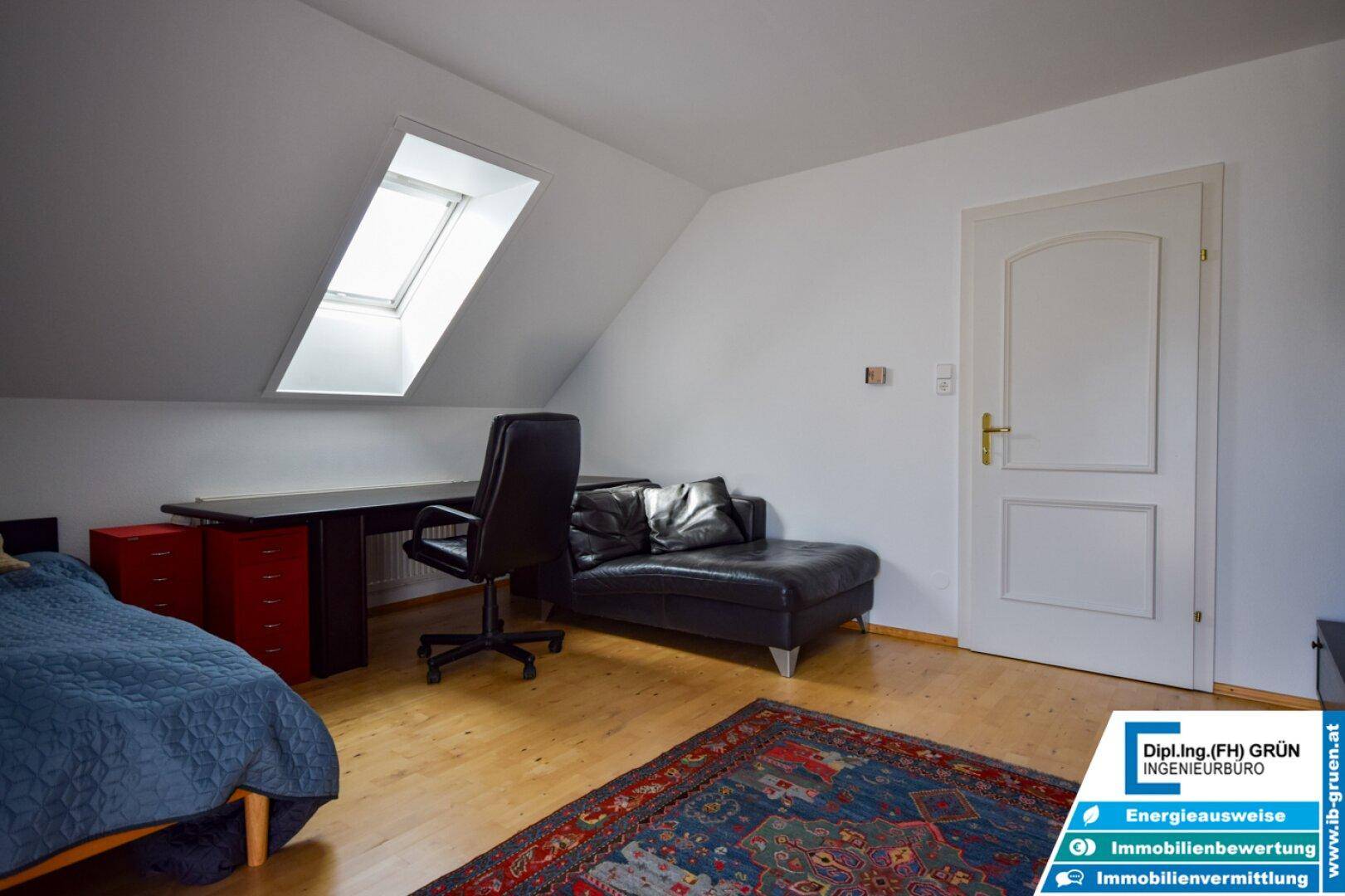 Schlafzimmer mit Schreibtisch, Liege und Dachfenster im oberen Stockwerk mit Holzboden.