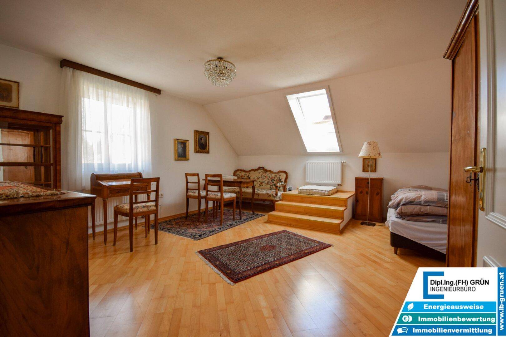 Helles Zimmer im Dachgeschoss mit Holzboden, Dachfenster und traditionellen Möbeln.