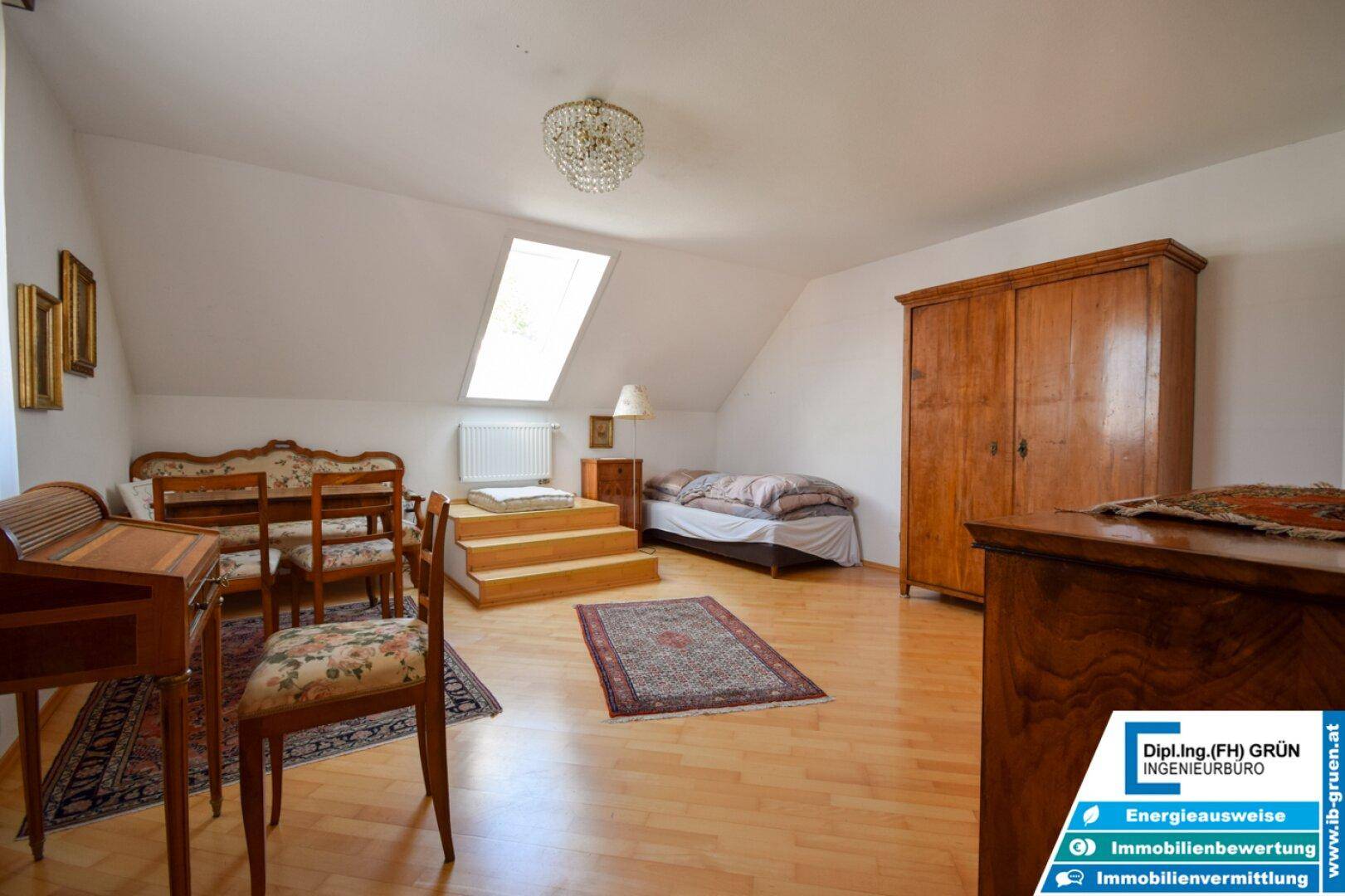 Dachgeschosszimmer mit Holzboden, Dachfenster und antiken Holzmöbeln, hell und geräumig.