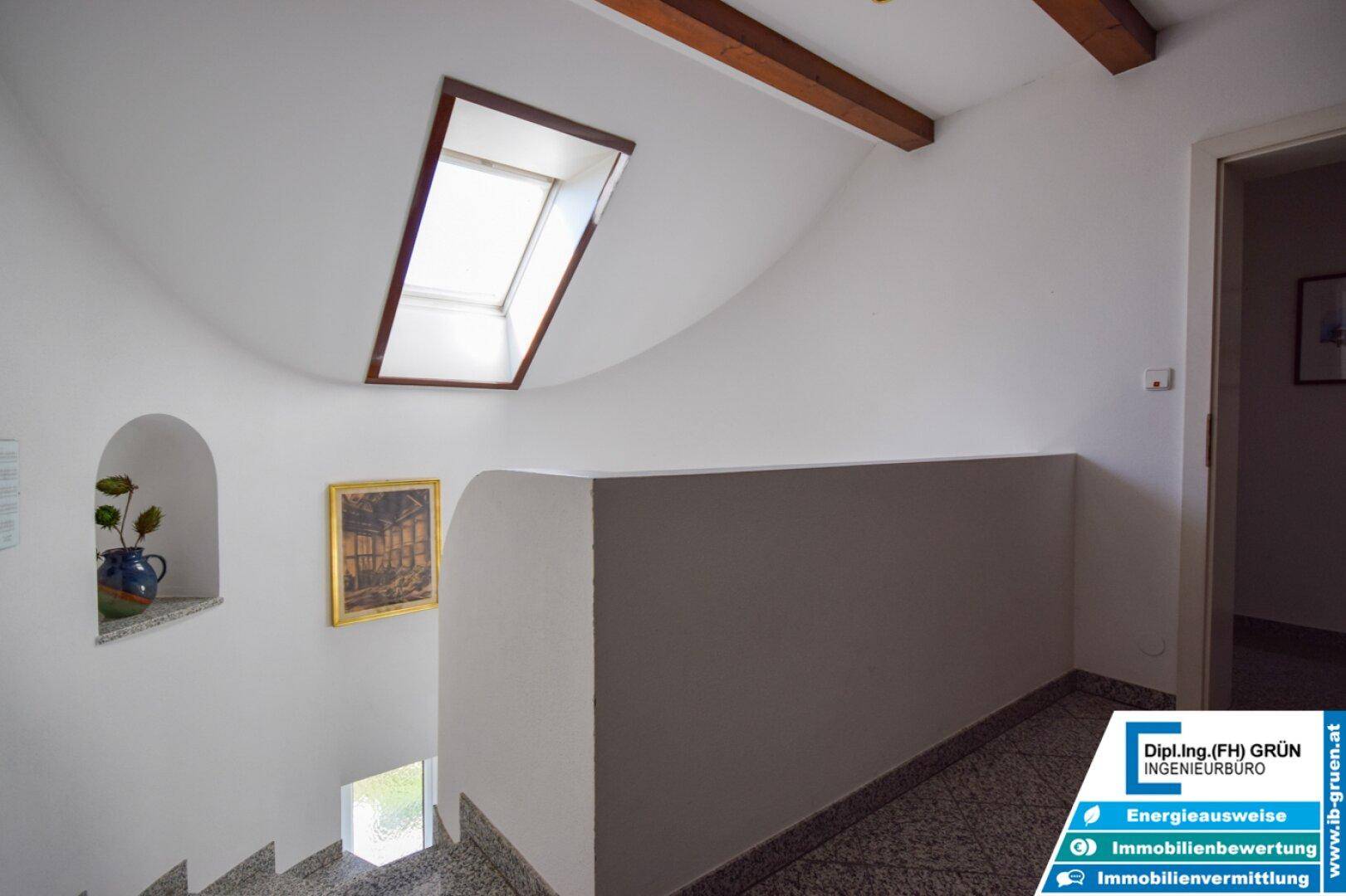 Treppenhaus mit Fliesenboden, Dachfenster und weiß gestrichenen Wänden, gut beleuchtet.