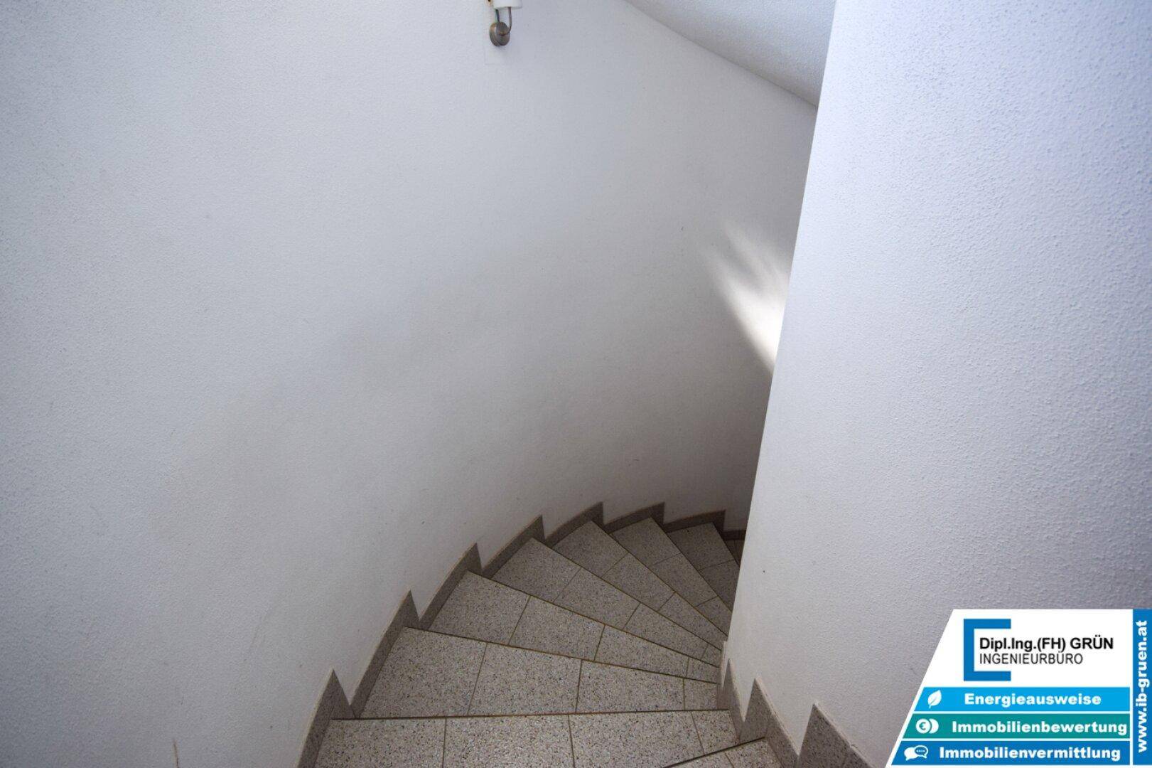 Wendeltreppe mit Fliesenstufen und weiß gestrichenen Wänden, führt in die oberen Etagen.