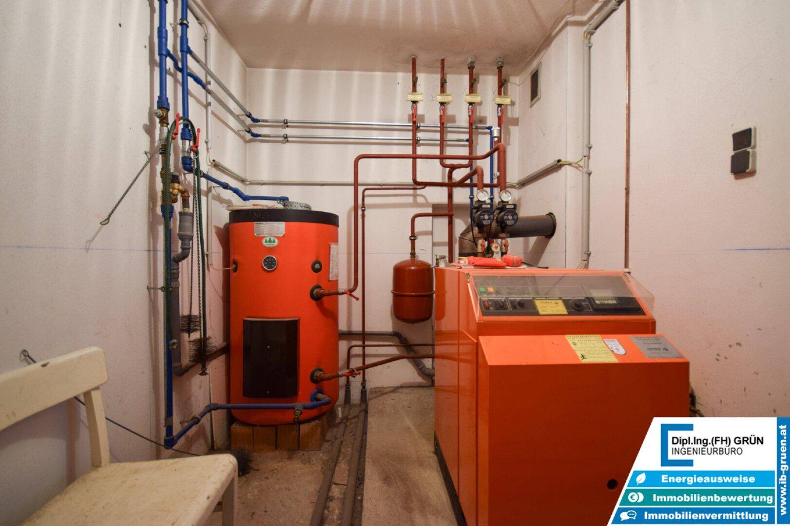Heizungsanlage mit orangefarbenem Boiler und Verrohrung in einem Kellerraum.
