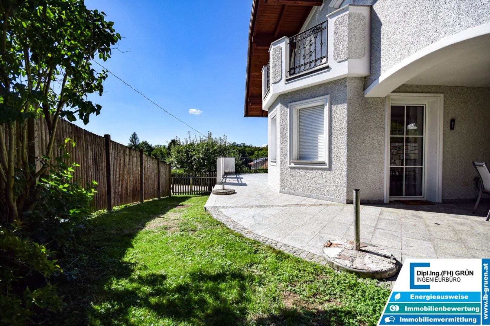 Gepflegter Gartenbereich mit Rasenfläche, gepflasterter Terrasse und Holzzaun.