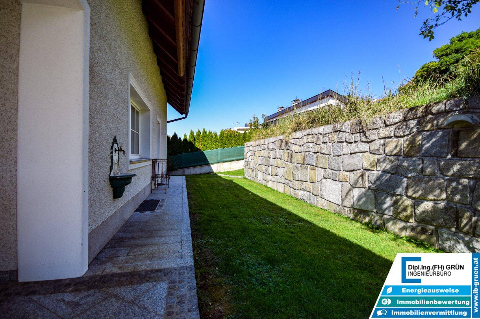 Seitlicher Gartenbereich mit Rasenfläche und einer robusten Steinmauer.