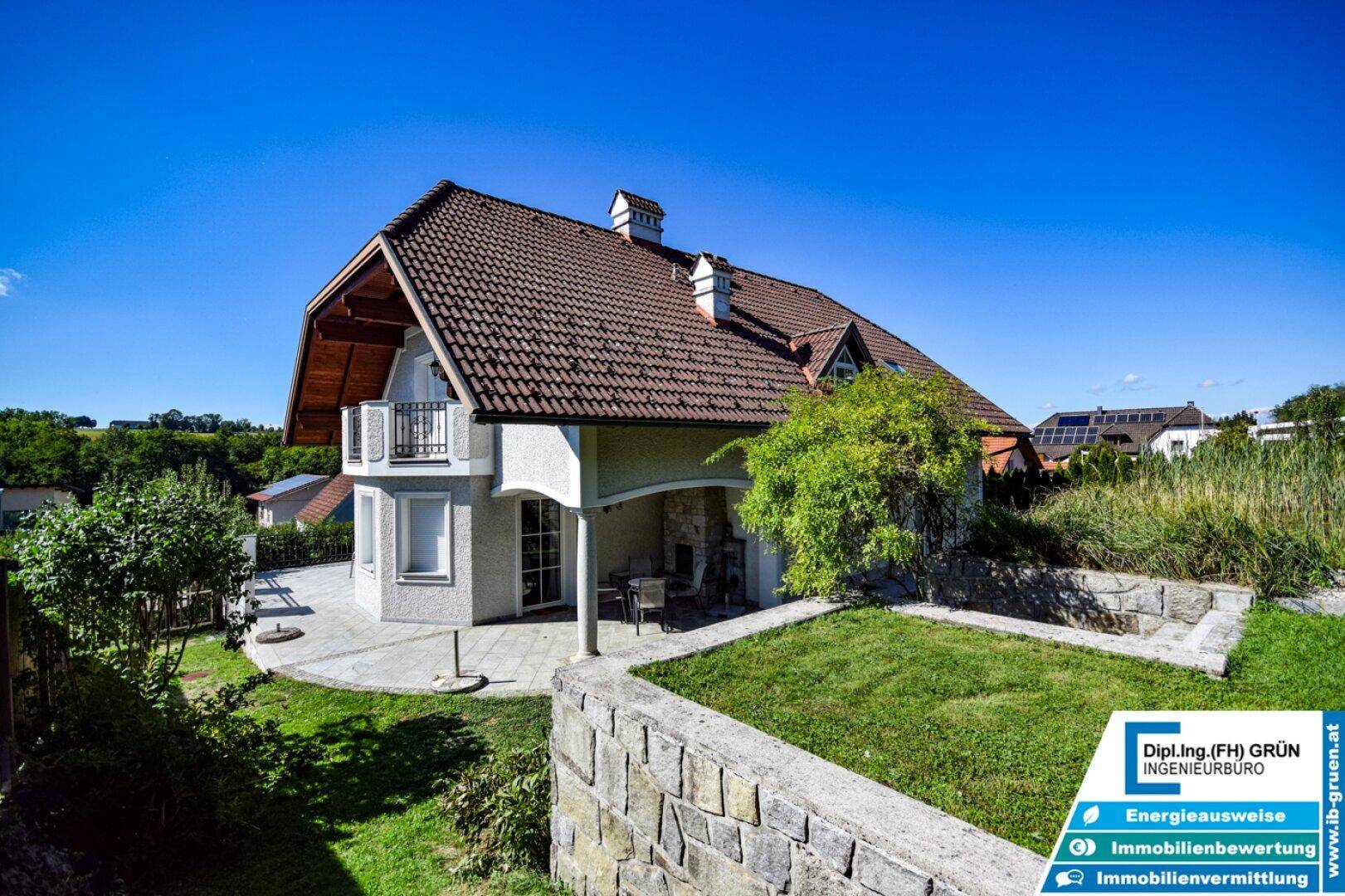 Hausansicht vom Garten aus mit Terrasse, Rasenfläche und Steinmauer.