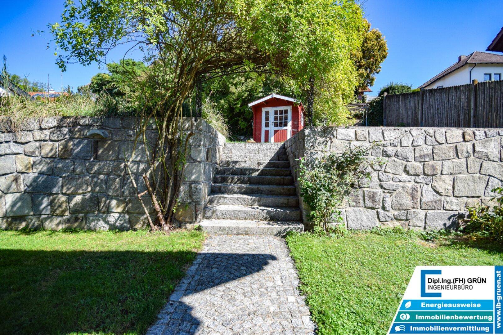 Gartenweg führt über Steinstufen zu einem charmanten roten Gartenhaus.