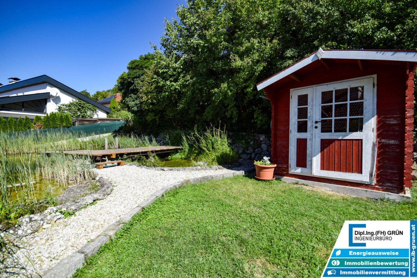 Idyllischer Gartenbereich mit rotem Gartenhaus, Teich und Kiesweg.