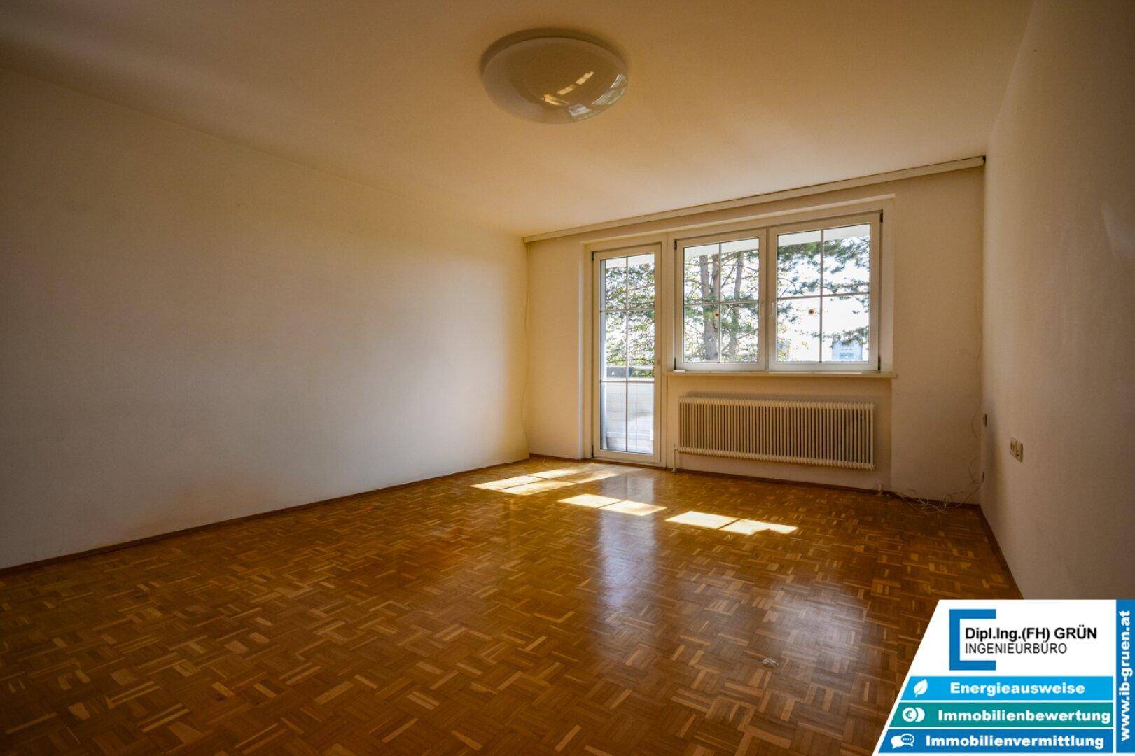 Heller, leerer Raum mit Parkettboden und Zugang zu einem Balkon.