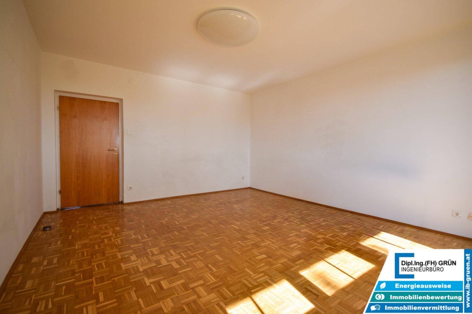 Leerer Raum mit Parkettboden und weiß gestrichenen Wänden.