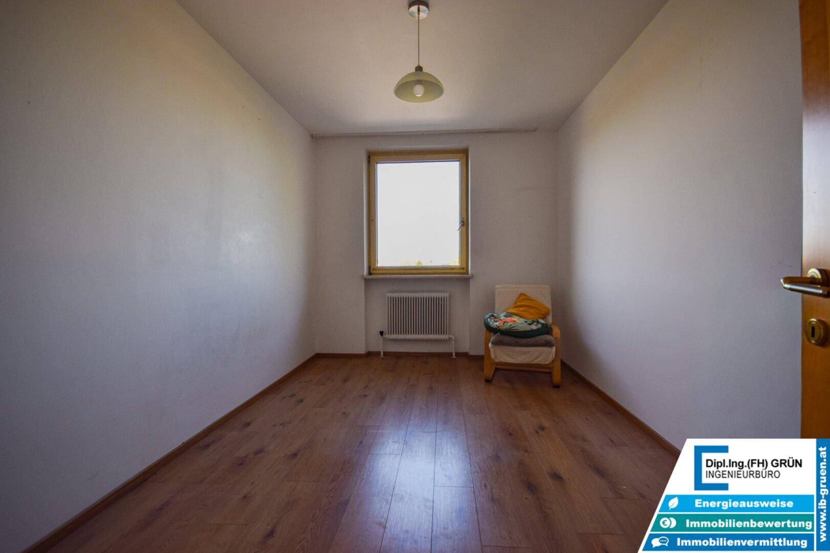 Leerer Raum mit Laminatboden und einem Fenster, das Tageslicht hereinlässt.