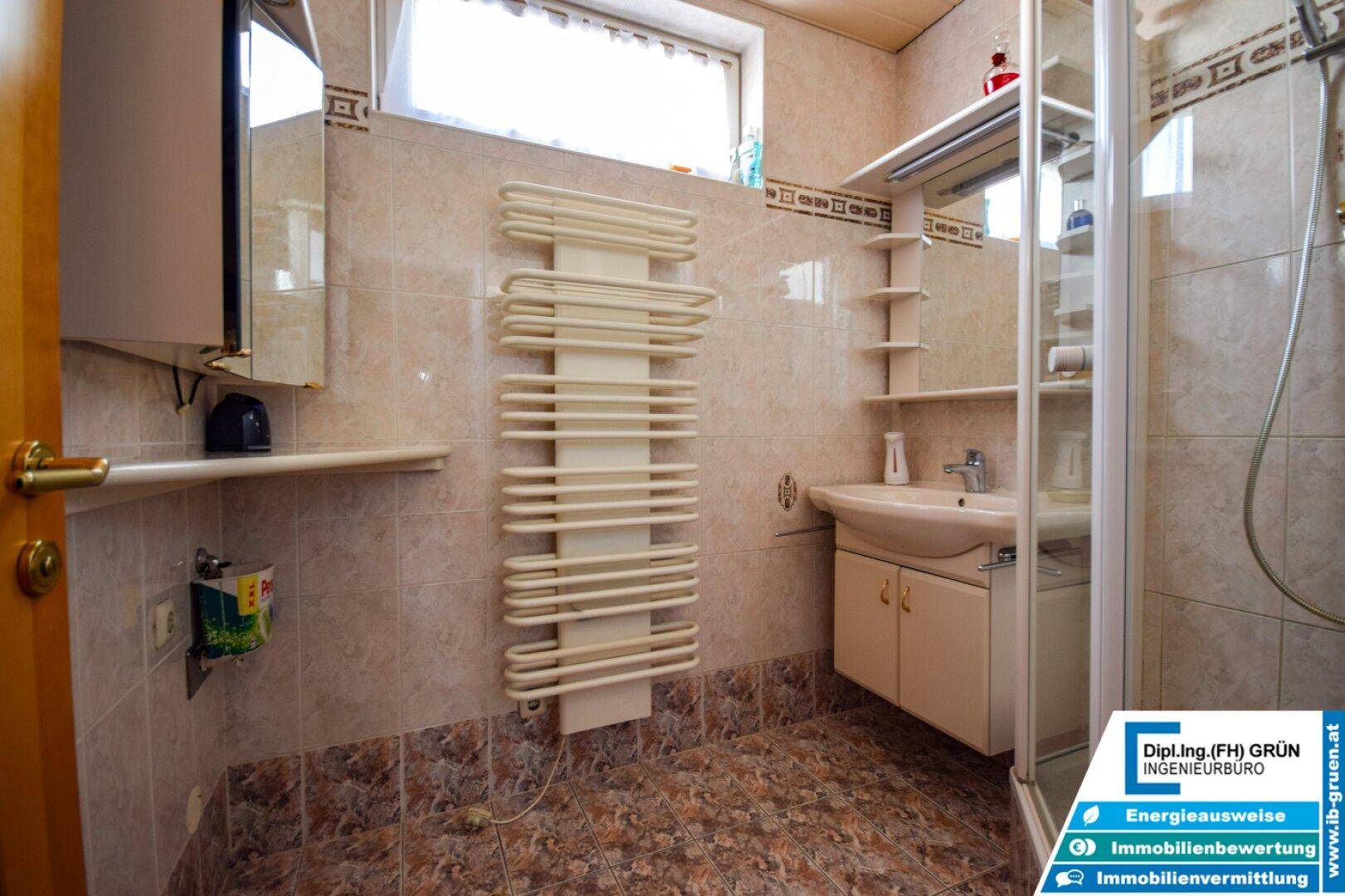 Badezimmer mit Duschkabine, Waschbecken, beheiztem Handtuchhalter und Fenster.