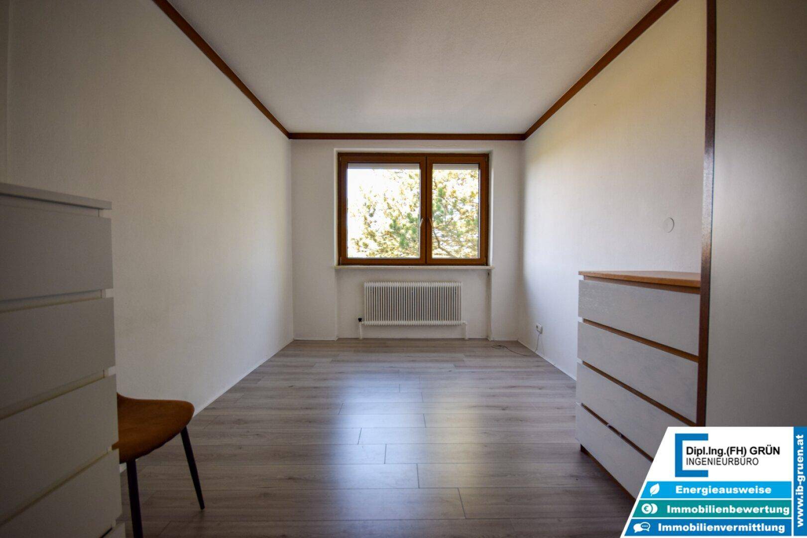 Leeres Schlafzimmer mit Laminatboden, Fenster und einer Kommode.