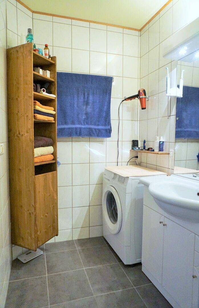 Badezimmer mit Waschmaschine, Waschbecken, Spiegel und einem hohen Holzschrank.