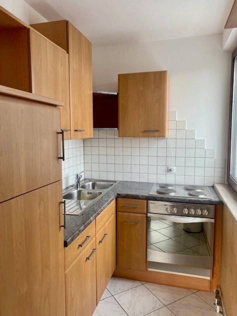 Funktionale Küche mit Holzschränken, Spüle, Elektroherd und weiß gefliestem Spritzschutz.