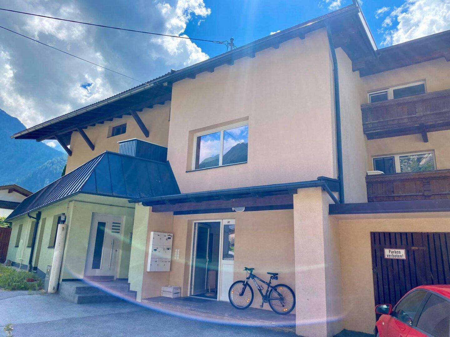 Fassade eines Wohnhauses mit Eingangsbereich, Balkonen und einem Fahrrad vor der Tür.