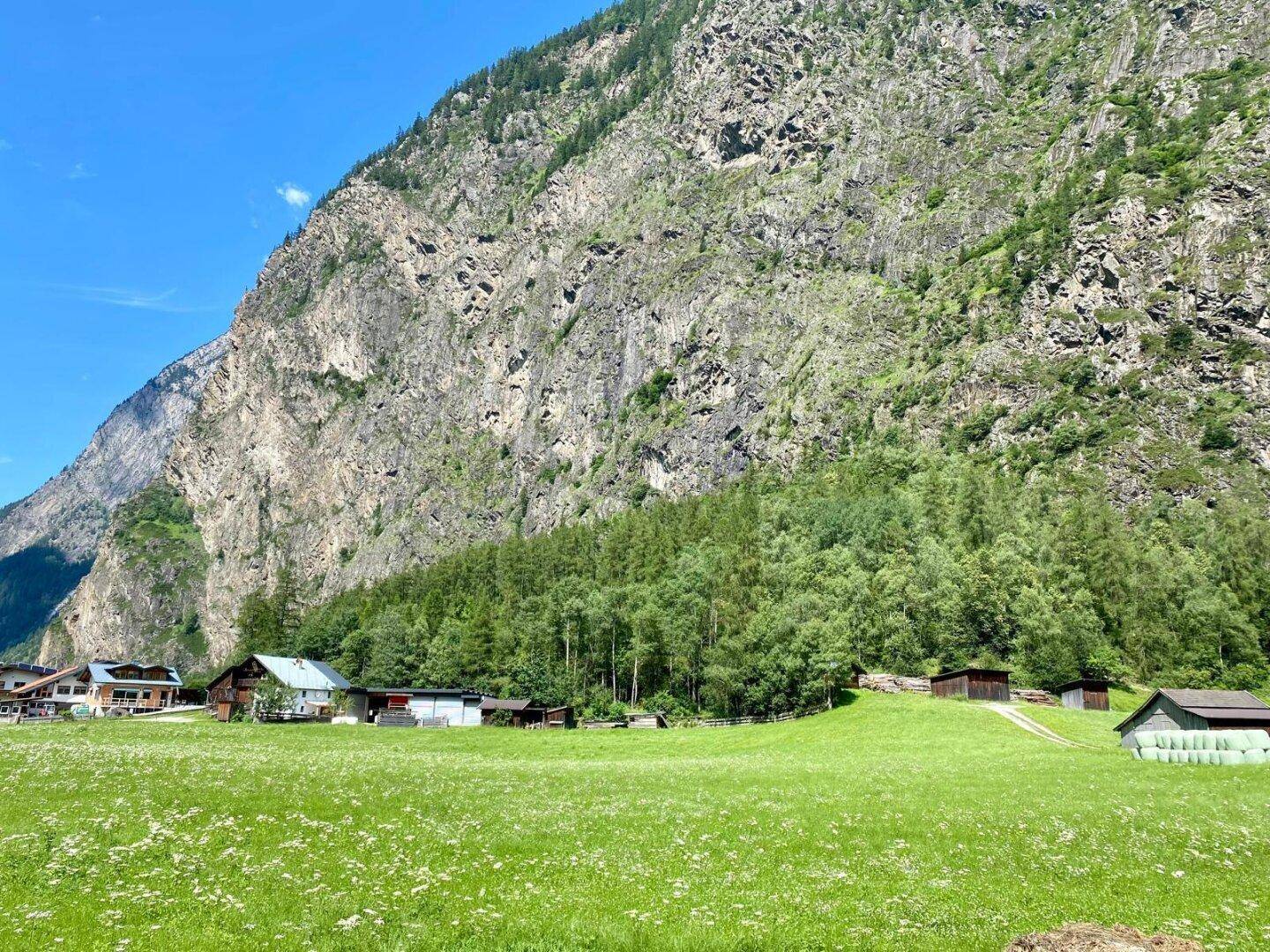 Weite Landschaft mit imposantem Berg, grünen Wiesen und vereinzelten Häusern am Horizont.